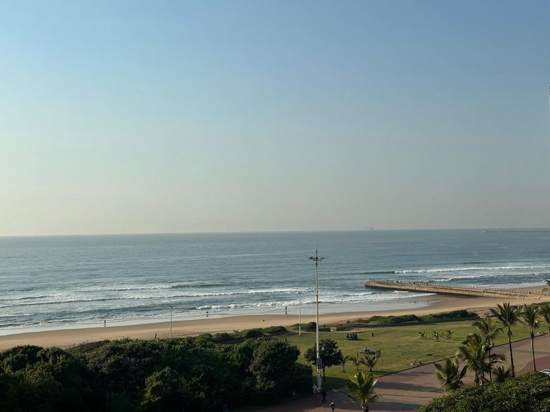 A scenic elevated view overlooking the coastline, sandy beach, and adjacent public parkland area.