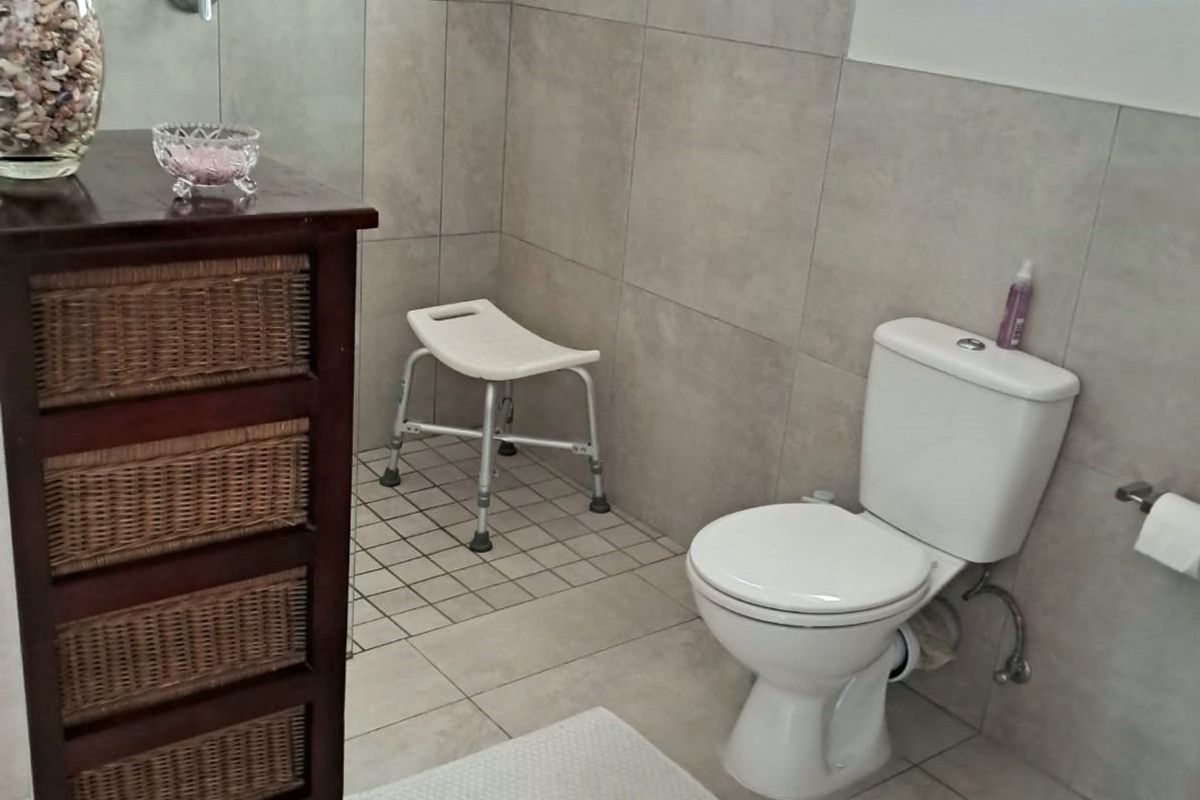 A clean, modern bathroom featuring neutral wall and floor tiles, a standard toilet, and a dedicated shower area with casement windows for natural light.