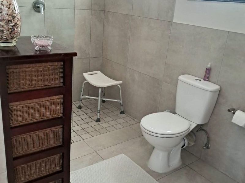 A clean, modern bathroom featuring neutral wall and floor tiles, a standard toilet, and a dedicated shower area with casement windows for natural light.