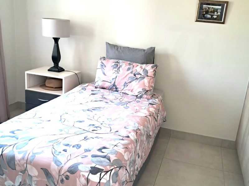 A compact bedroom featuring neutral tiled flooring and plain walls, providing a simple and functional sleeping space.