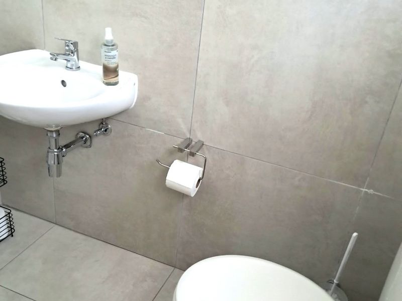 A modern, well-maintained bathroom featuring large format neutral tiling, a wall-mounted basin with chrome fixtures, and a standard toilet.