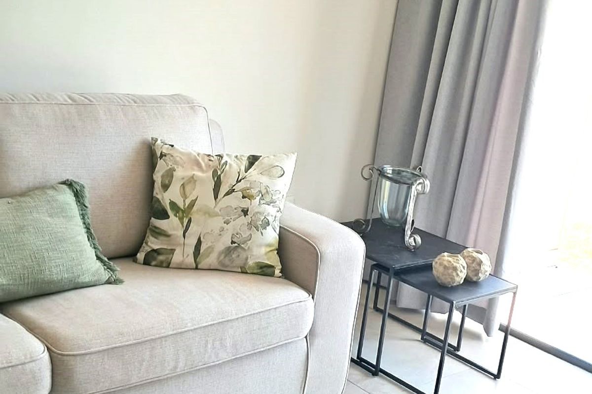 A bright living room area featuring neutral tiled flooring and a large sliding glass door with floor-to-ceiling curtains.