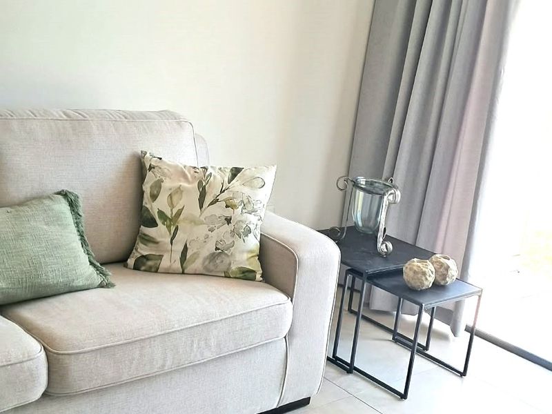 A bright living room area featuring neutral tiled flooring and a large sliding glass door with floor-to-ceiling curtains.