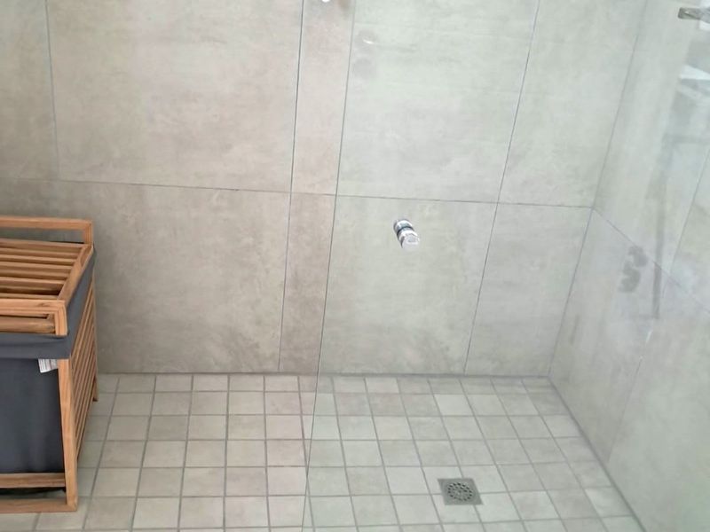 A modern walk-in shower featuring neutral-toned wall and floor tiles with a frameless glass screen and chrome mixer tap.