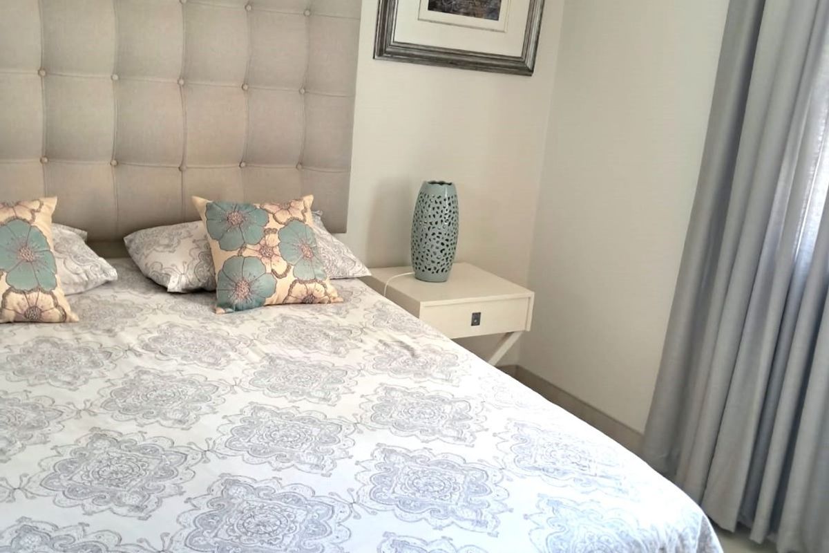 A well-maintained bedroom featuring neutral wall tones, tiled flooring, and a wall-mounted air conditioning unit.