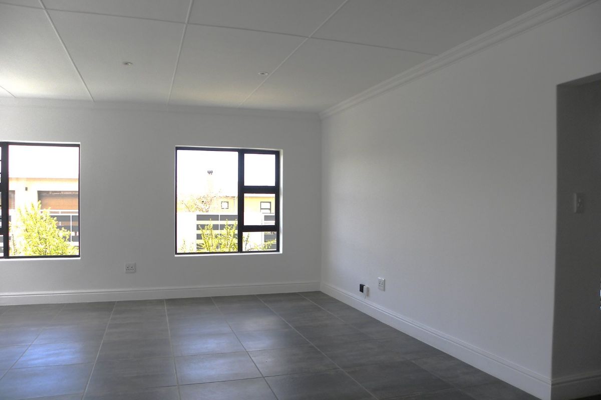A bright, empty living room featuring modern grey floor tiles, recessed ceiling lighting, and large aluminium-framed windows.