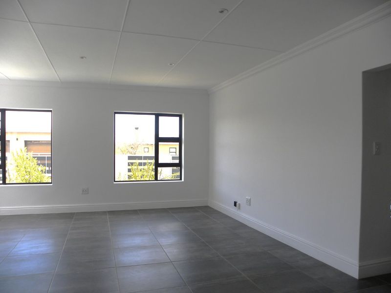 A bright, empty living room featuring modern grey floor tiles, recessed ceiling lighting, and large aluminium-framed windows.
