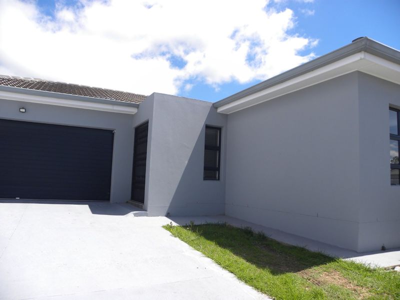 Modern exterior view of the property featuring a clean grey facade, a secure garage entrance, and a paved driveway with a small lawn area.