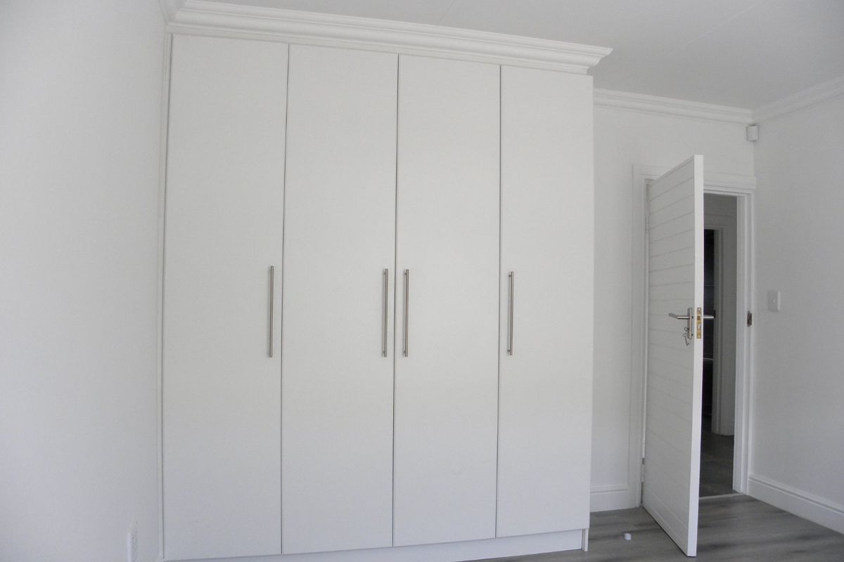 A clean, modern bedroom featuring white built-in cupboards, crown molding, and grey laminate flooring.