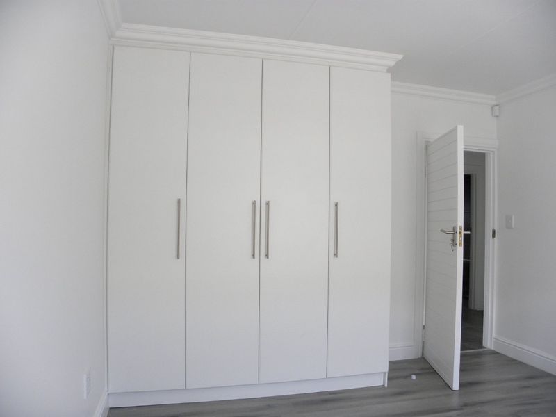 A clean, modern bedroom featuring white built-in cupboards, crown molding, and grey laminate flooring.