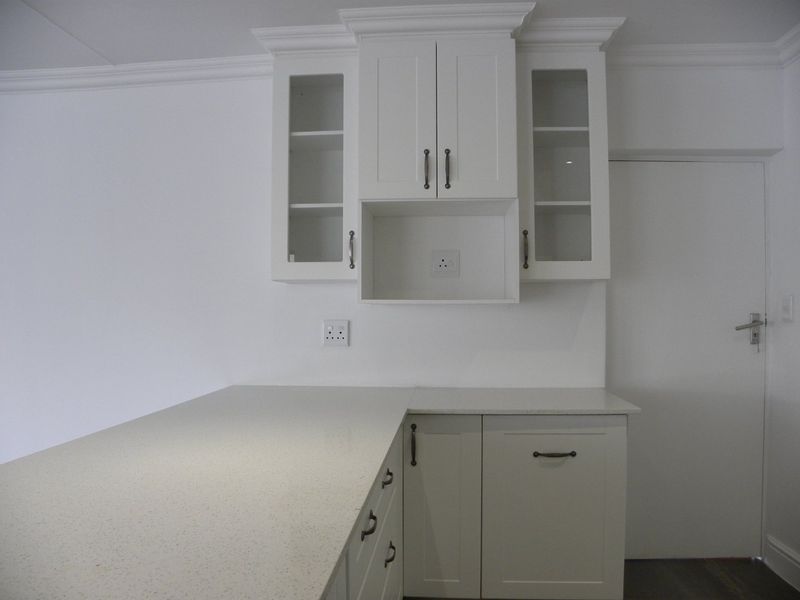 A clean, modern kitchen area featuring white shaker-style cabinetry, glass-front upper cabinets, and light-colored quartz countertops with integrated electrical points.
