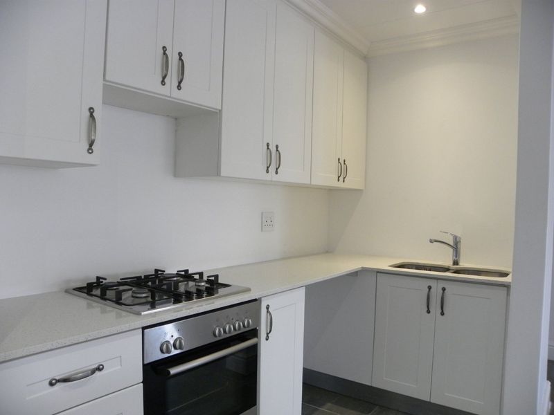 A clean, modern kitchen featuring white cabinetry, stone countertops, a gas hob, an integrated oven, and a stainless steel sink.