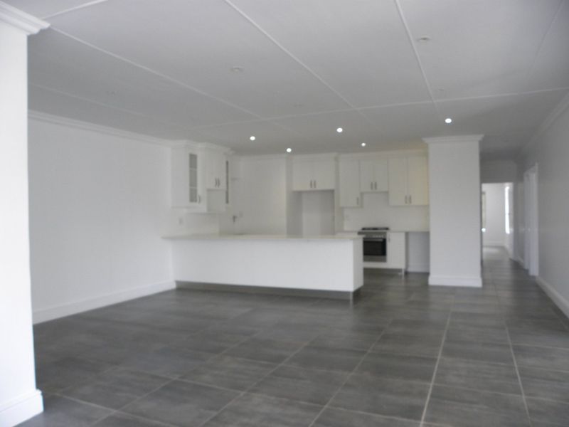 Spacious open-plan living area featuring a modern kitchen with built-in cabinetry, oven, hob, and large format floor tiles throughout.