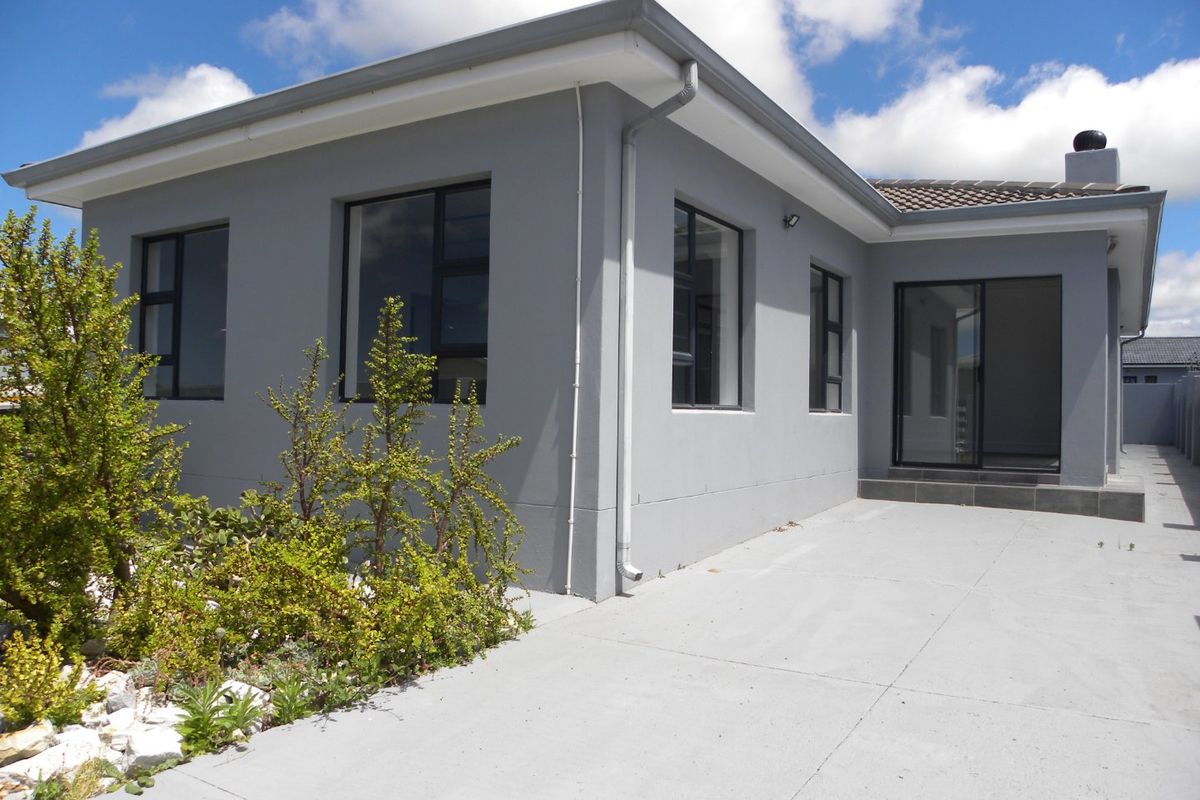 Rear view of the house featuring a concrete patio, modern grey exterior walls, aluminium window frames, and a sliding glass door entrance.