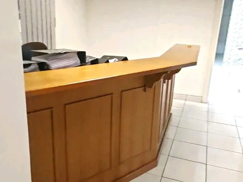 A commercial entry area featuring a built-in wooden reception desk and tiled flooring, providing a functional welcome space for clients.
