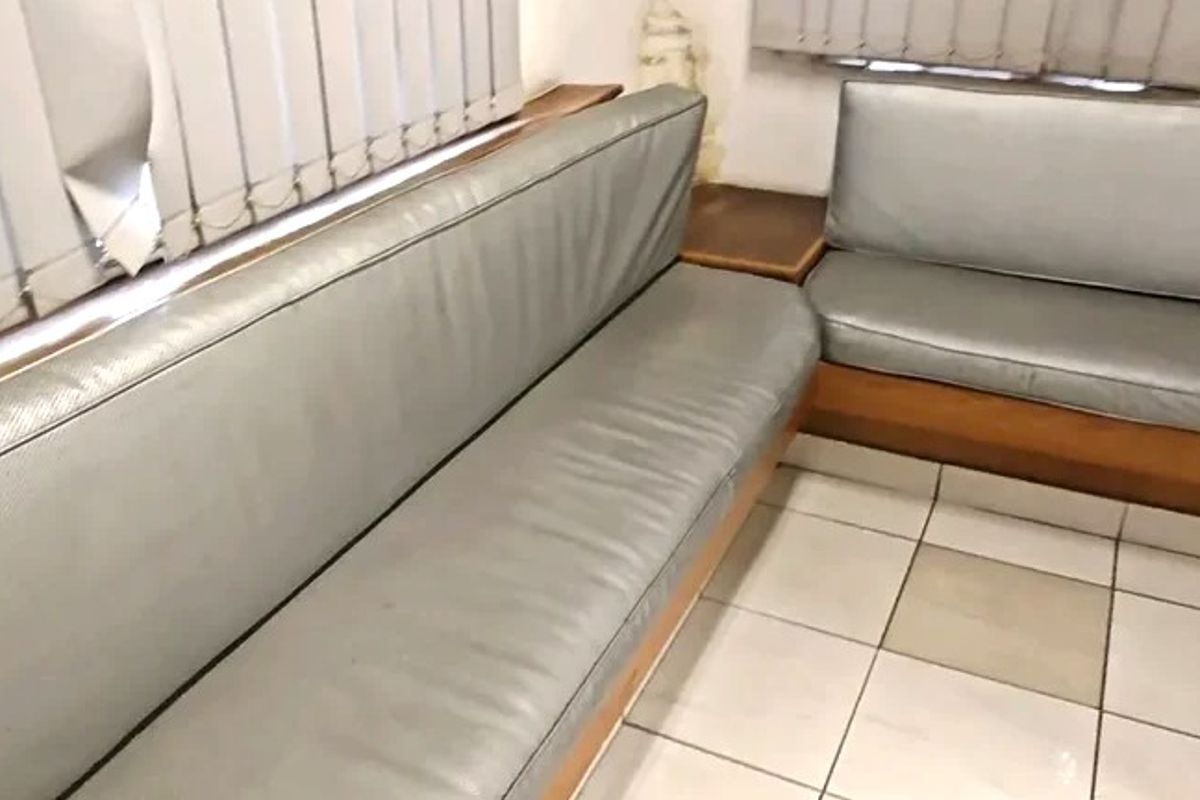 A commercial waiting area featuring built-in bench seating, ceramic tile flooring, and vertical blinds, showing signs of wear and minor wall damage.