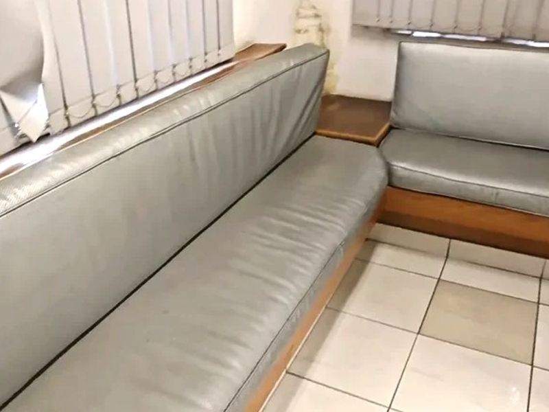 A commercial waiting area featuring built-in bench seating, ceramic tile flooring, and vertical blinds, showing signs of wear and minor wall damage.