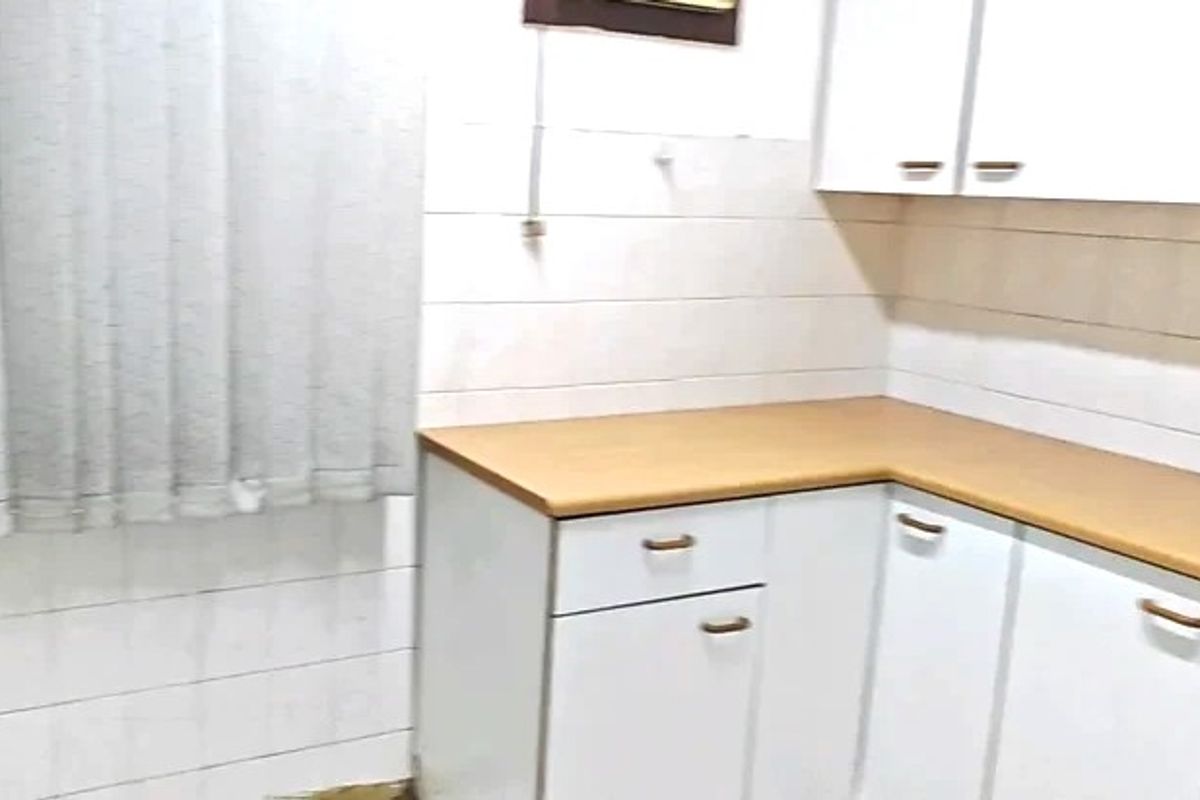 A compact kitchen area featuring white cabinetry, laminate countertops, and tiled wall finishes, currently in need of cosmetic updates and maintenance.