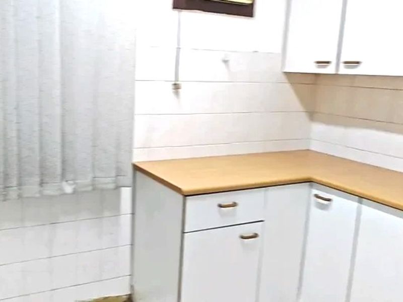 A compact kitchen area featuring white cabinetry, laminate countertops, and tiled wall finishes, currently in need of cosmetic updates and maintenance.
