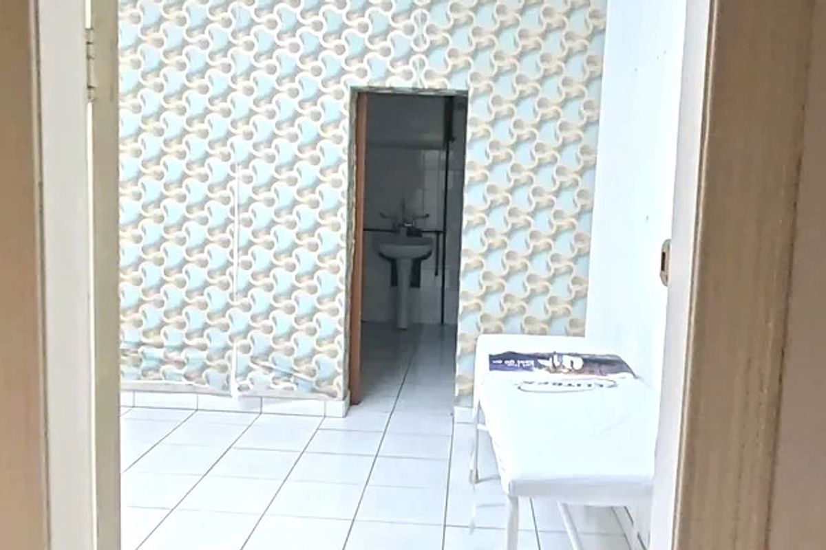 A small commercial bathroom space featuring a pedestal sink, white ceramic floor tiles, and dated patterned wallpaper in need of refurbishment.