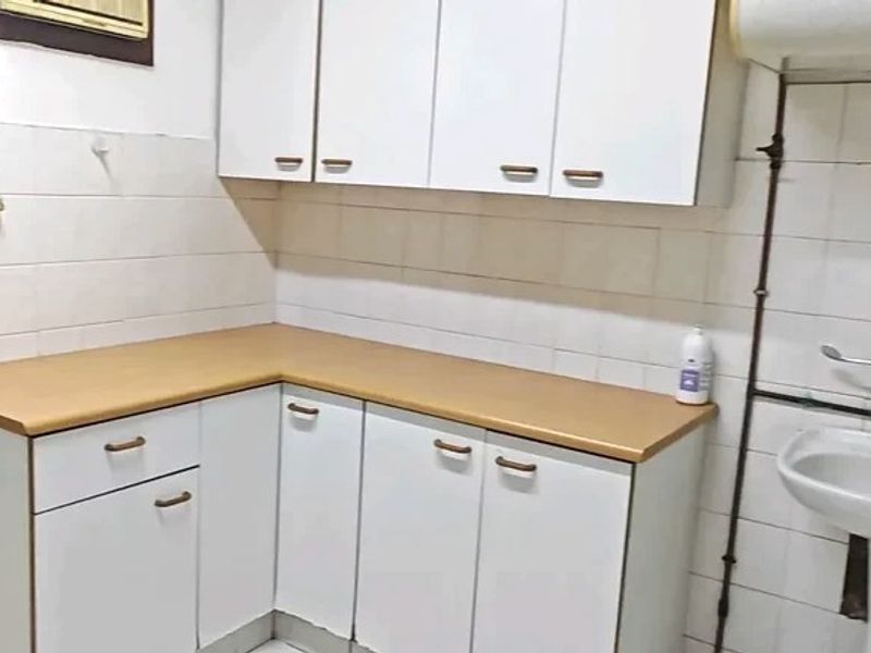 A functional scullery or utility area featuring white built-in cabinetry, a laminate countertop, and a pedestal sink with exposed plumbing.