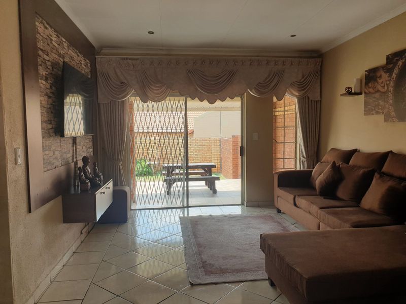 A living room featuring tiled flooring, a stone feature wall, and a sliding glass door with a security gate leading to the patio.