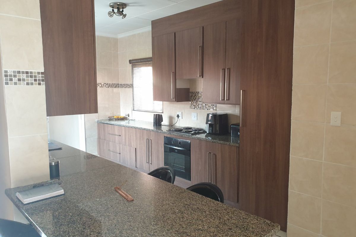 A functional kitchen featuring dark wood cabinetry, granite countertops, a breakfast bar, and integrated oven and hob with a tiled backsplash.