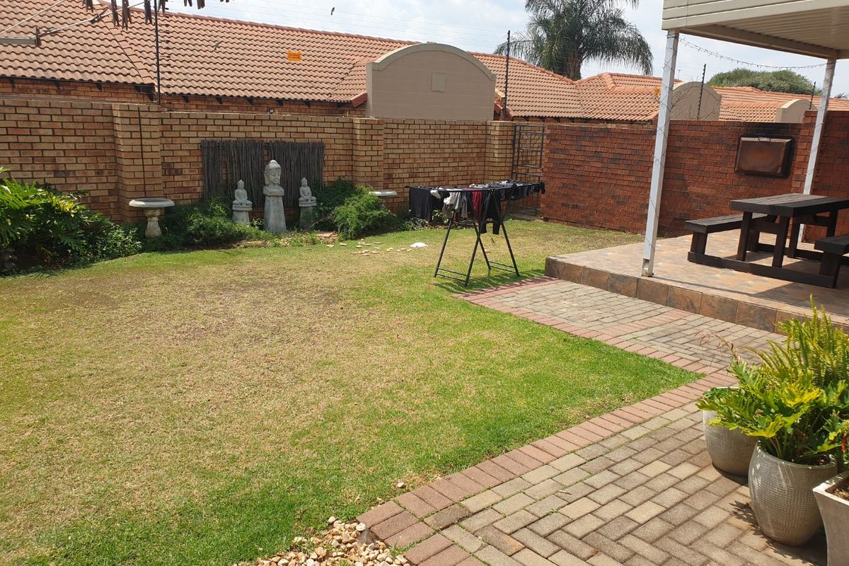 A private rear garden featuring a paved patio area, a covered outdoor space with a built-in braai, and a well-maintained lawn.