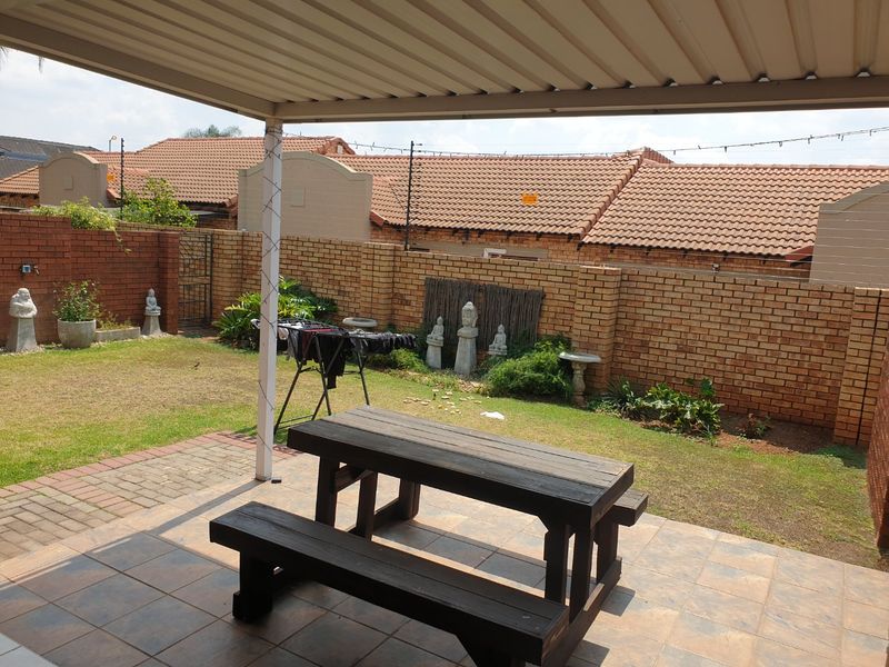 A covered patio area with tiled flooring, overlooking a private garden enclosed by a brick boundary wall.