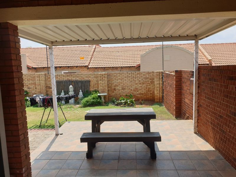 A covered outdoor patio area featuring tiled flooring and a brick boundary wall, overlooking a private garden space.
