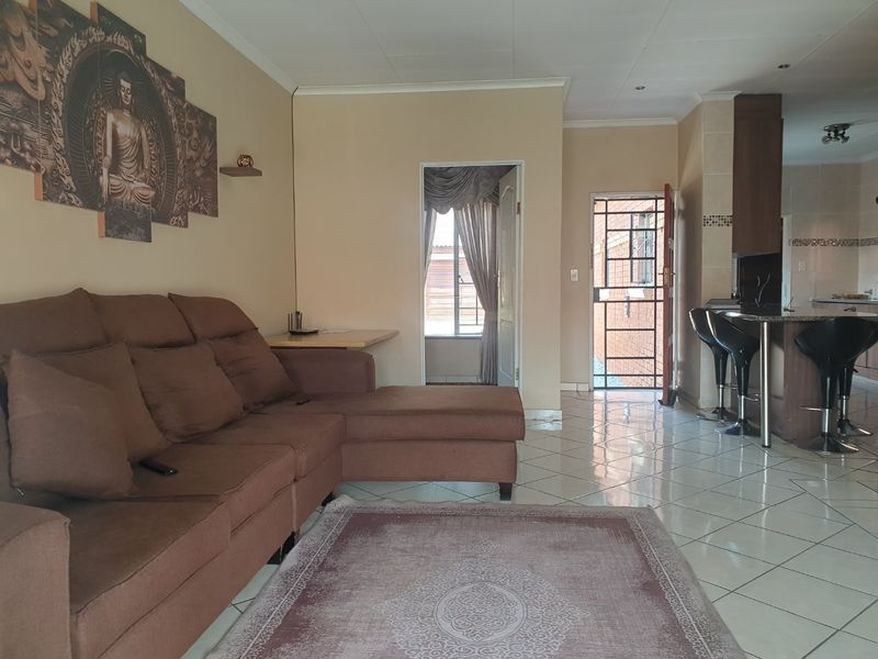 Open-plan living area featuring tiled flooring, a kitchen breakfast bar, and direct access to the exterior through a security gate.