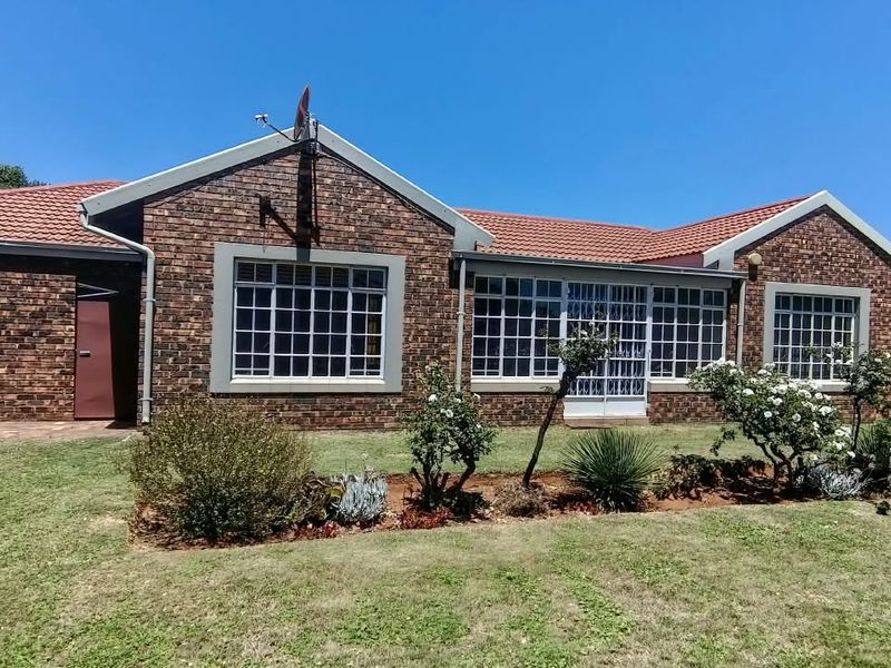 A well-maintained rear exterior view of a face brick townhouse featuring a tiled roof, grid windows, and a landscaped garden area.