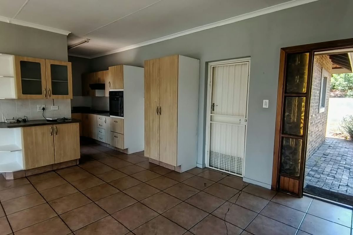 A functional kitchen featuring light wood-finish cabinetry, built-in oven, and tiled flooring, with direct access to an outdoor paved area.