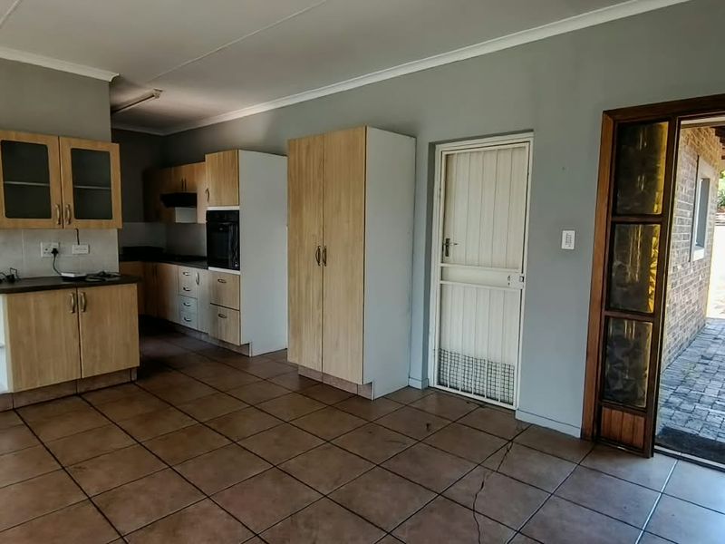 A functional kitchen featuring light wood-finish cabinetry, built-in oven, and tiled flooring, with direct access to an outdoor paved area.
