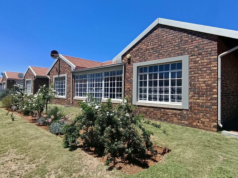 A well-maintained townhouse exterior featuring face brick construction, a tiled roof, and large grid-pattern windows overlooking a neat garden area.