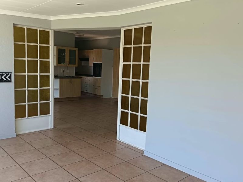 An open-plan living area featuring tiled flooring and french doors leading to a kitchen with built-in cabinetry and appliances.