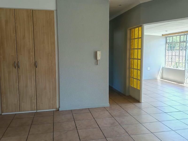 An empty living area featuring tiled flooring, built-in storage cupboards, and a decorative glass panel divider leading to an adjacent sunroom space.