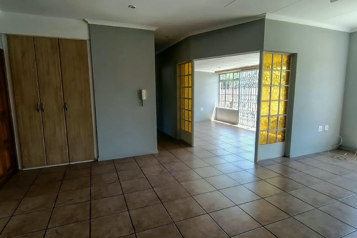 Spacious living area featuring tiled flooring, built-in storage, and a decorative glass partition leading to an adjacent room with security gate access.