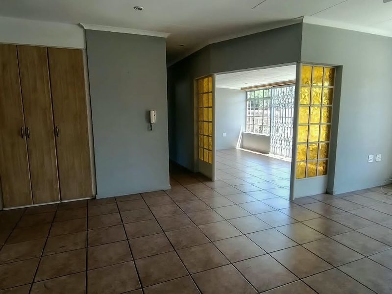 Spacious living area featuring tiled flooring, built-in storage, and a decorative glass partition leading to an adjacent room with security gate access.