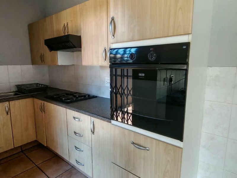 A functional kitchen featuring light wood cabinetry, built-in oven, gas hob, extractor fan, and tiled finishes throughout.