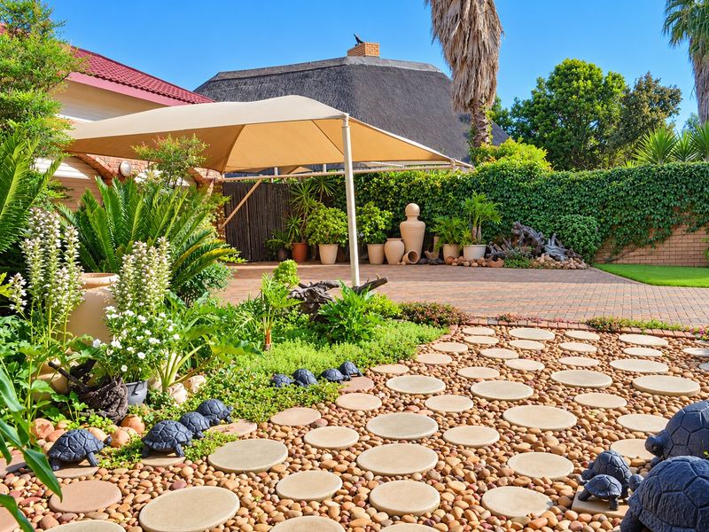 A well-maintained rear garden area featuring a paved driveway, decorative pebble landscaping with stepping stones, and a functional shade sail structure.