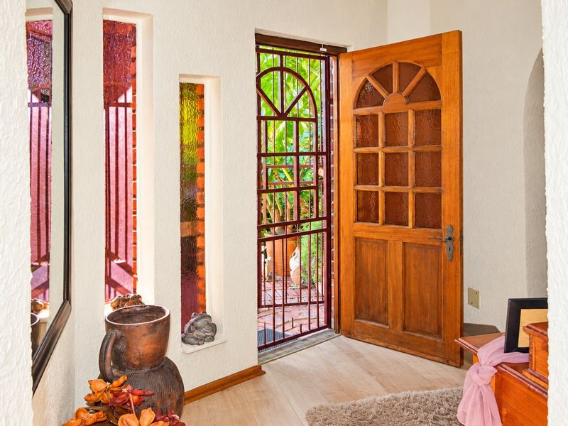 Welcoming entrance area featuring a solid timber door with glass panels, security gate, and textured walls leading to an outdoor space.