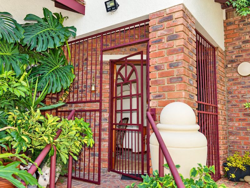 A secure entrance area featuring a brick facade, metal security gate, and paved walkway with handrails.