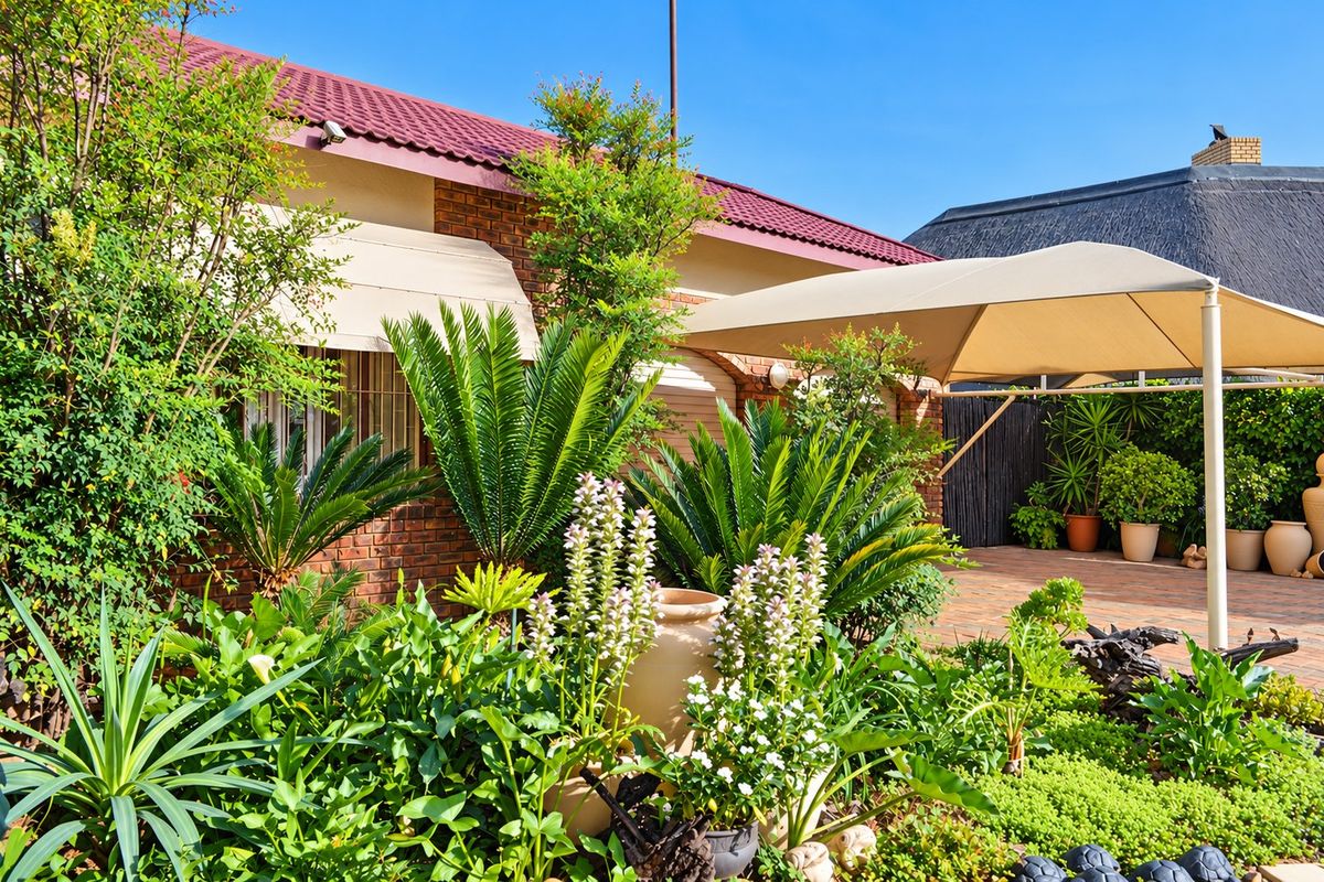 A well-maintained rear garden area featuring a paved patio with a shade awning, established landscaping, and a brick-faced house exterior.