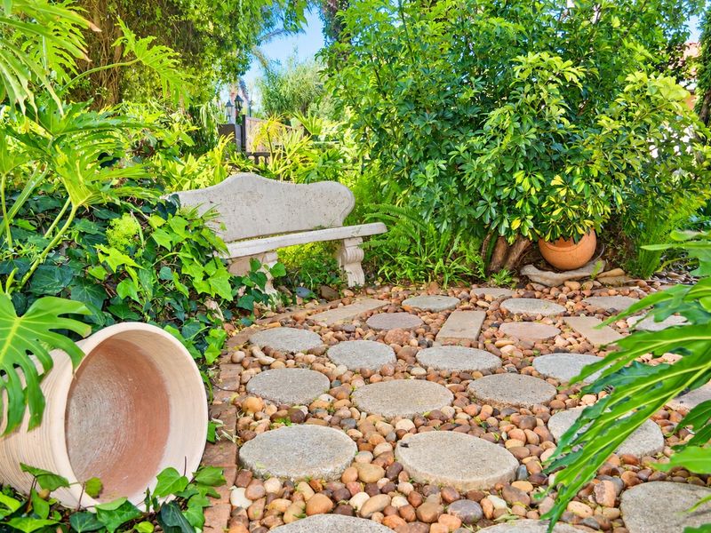 A lush, well-maintained garden area featuring a stone bench and a decorative pebble path with stone pavers.