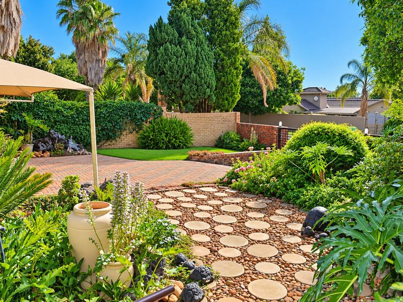 A beautifully landscaped rear garden featuring brick paving, decorative stepping stones, pebble beds, and established greenery enclosed by a brick boundary wall.