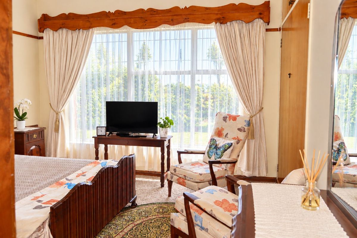 A well-lit bedroom featuring a large window with a decorative wooden pelmet and a built-in wardrobe, offering a comfortable and functional living space.