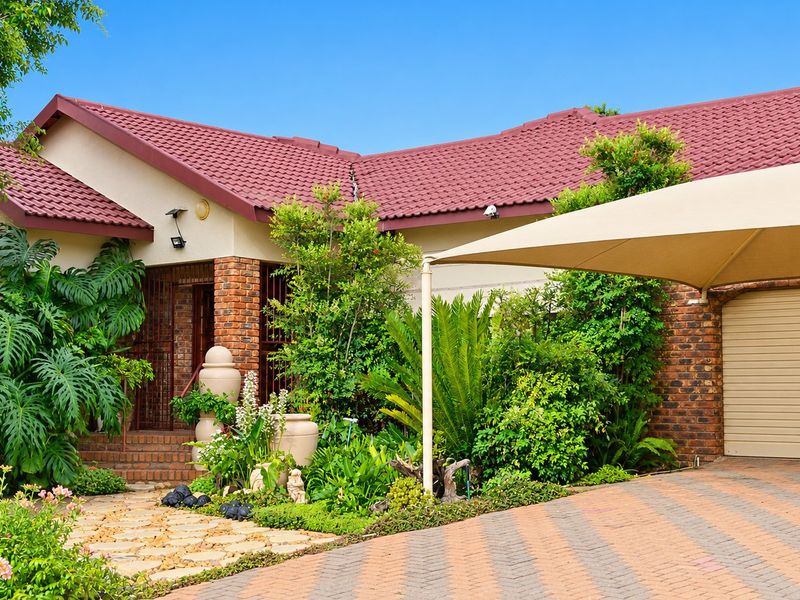 Front elevation of a house featuring a tiled roof, brick facade, paved driveway, and a shade sail over the garage entrance.