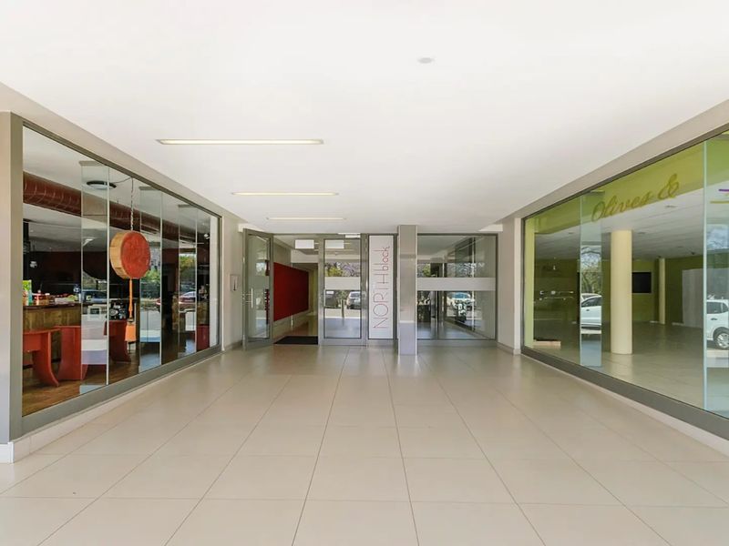 A bright and modern commercial building entrance lobby featuring large glass storefronts, tiled flooring, and recessed ceiling lighting.