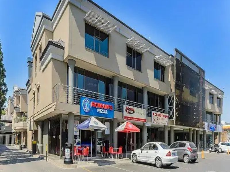 A multi-story commercial building featuring a paved parking area, balcony railings, and prominent storefront signage for various businesses.